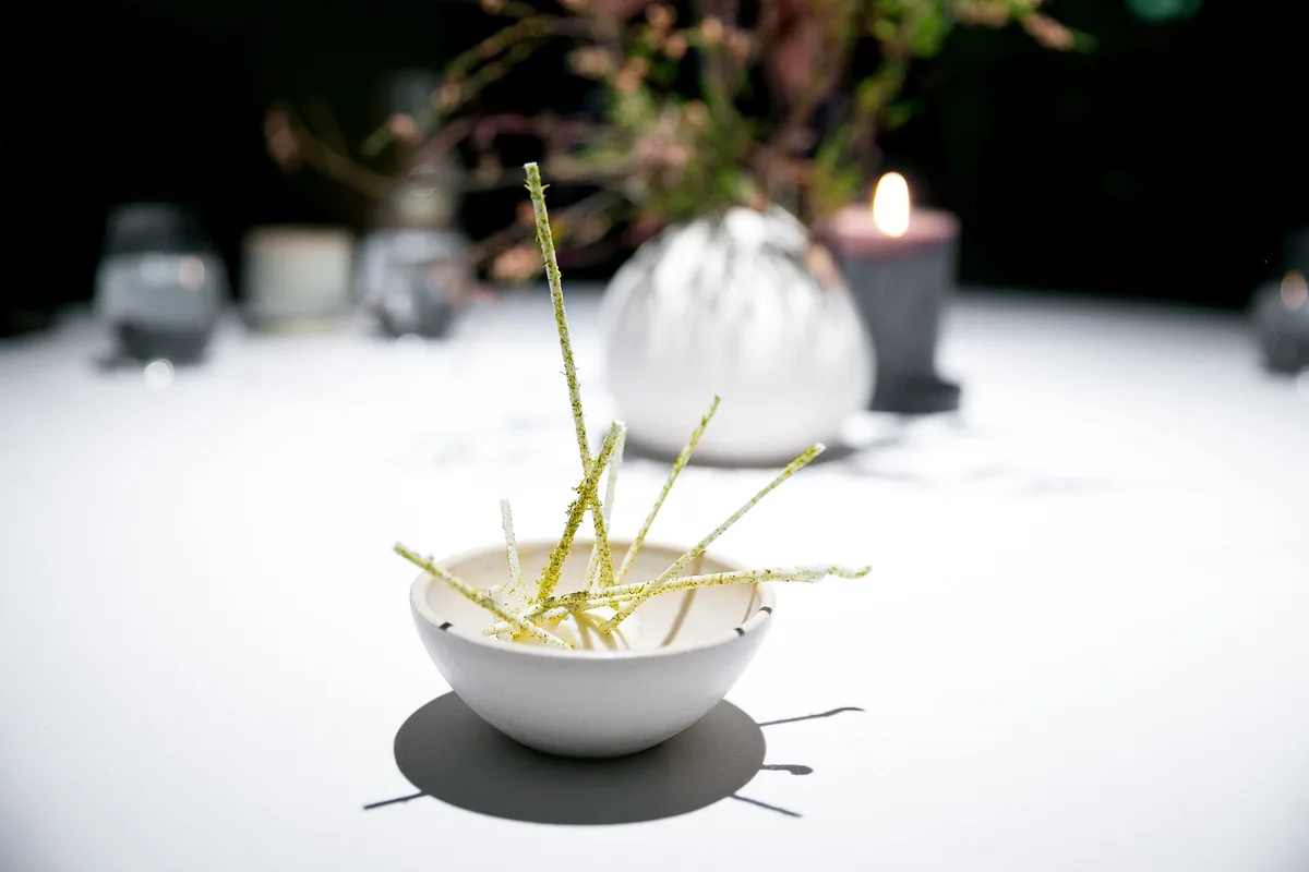 A course in a white bowl, with a candle and flowers on the table behind, at Maaemo, Oslo (photographed in 2015)