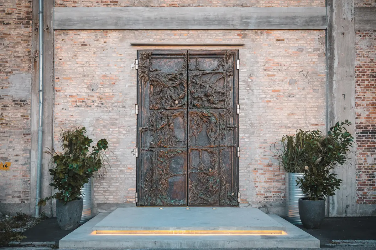 The tall wooden entrance doors of Alchemist, Copenhagen, flanked by potted plants