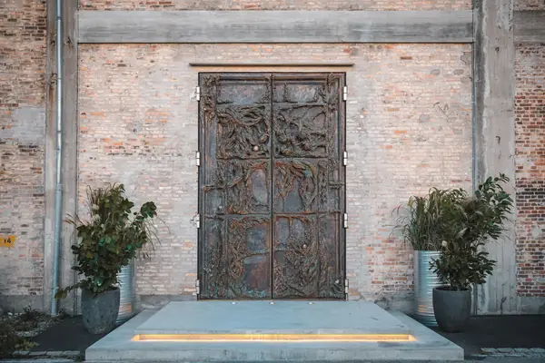 The tall wooden entrance doors of Alchemist, Copenhagen, flanked by potted plants