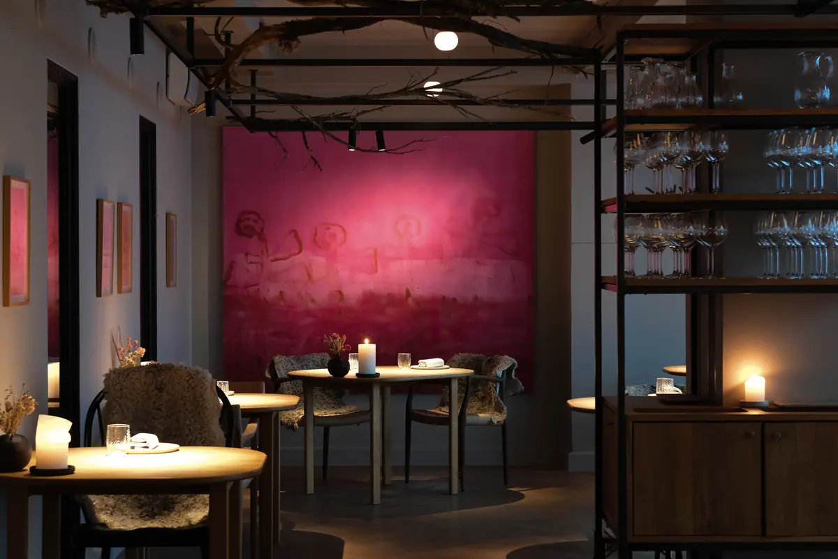 The candlelit dining room at Kadeau Copenhagen, with round tables in front of a deep-pink wall